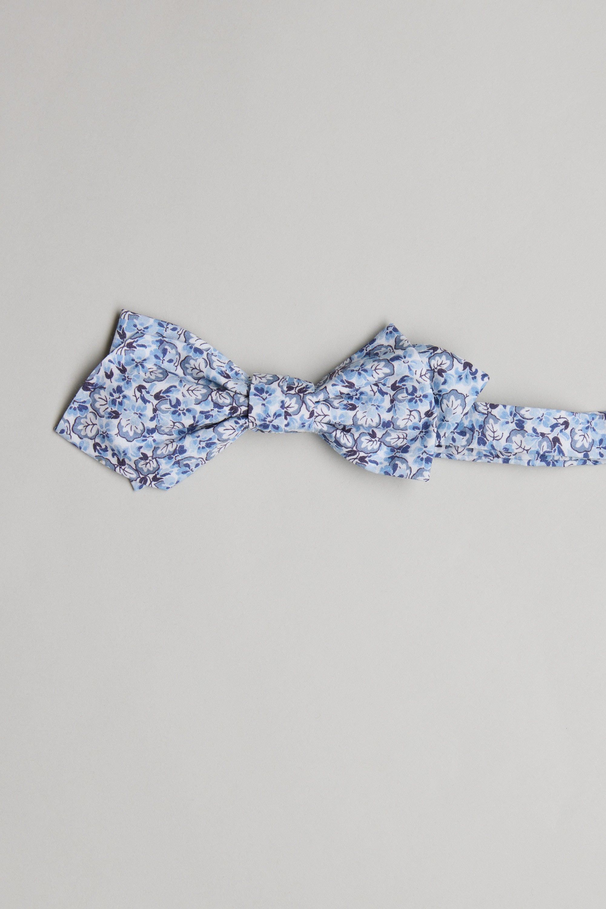 The Liberty Tommaso Bow Tie by Liberty features a light blue floral print in blue and white, handmade in New Zealand, and shown on a plain light grey background.