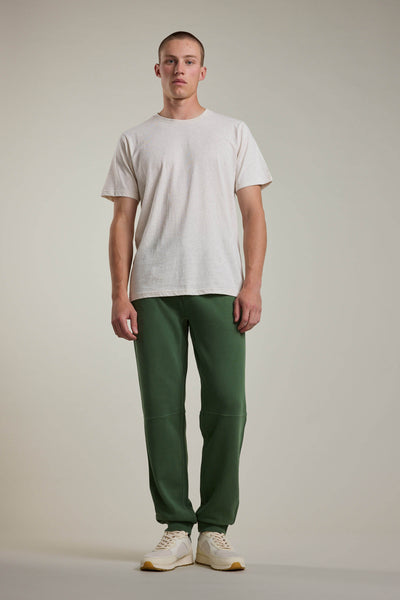 A man faces forward wearing a plain white T-shirt, Barkers Newton GD Track Pant in green, and white sneakers against a plain light background.