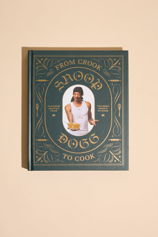 From Crook to Cook by Other is a hardcover cookbook with gold ornate designs on a dark green cover, featuring Snoop Dogg on the front and offering his collection of cannabis-free recipes.