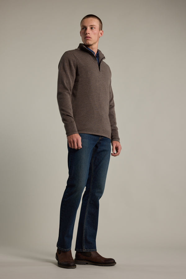 A man models the Barkers Brandon ZQRX Merino 1/4 Zip, styled with blue jeans and brown boots against a plain background. He stands relaxed, looking slightly to the side. Ideal as a versatile layering piece year-round.