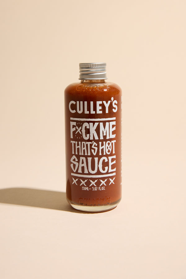 A bottle of Culley's F@#k Me That's Hot Sauce features bold white text on a light beige label. This New Zealand hot sauce packs Carolina Reaper heat in fiery red sauce, sealed with a metal cap.