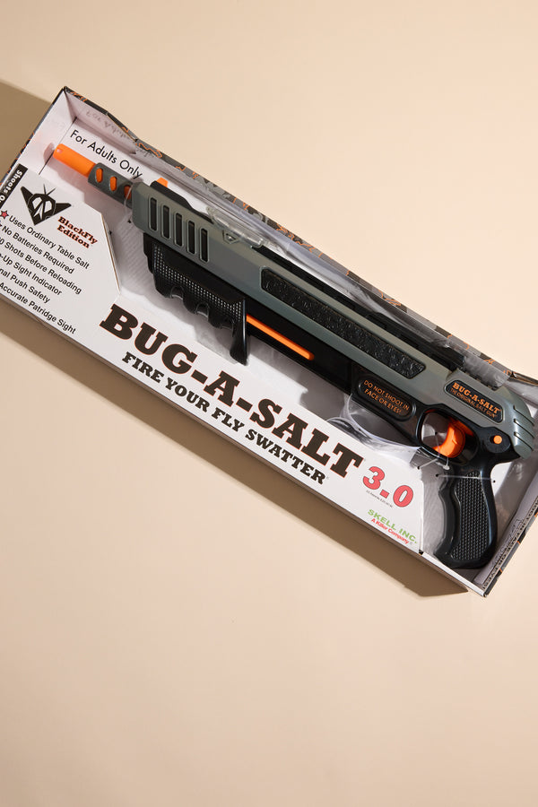 Boxed Bug-A-Salt 3.0 Black Fly by Other, an insect eradication device for shooting flies with salt, labeled “Fire Your Fly Swatter,” is displayed on a beige background. Packaging features usage and safety instructions.