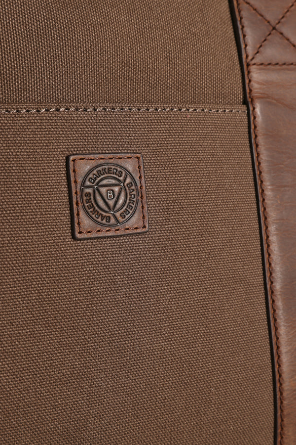 Close-up of the Newman Canvas Weekender, a brown canvas and leather travel bag by Barkers, featuring a stitched rectangular Barkers brand patch with a circular emblem in the center.