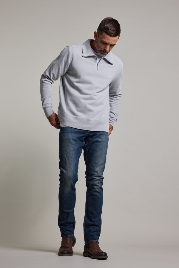 A man with short hair and a trimmed beard wears the Barkers Galway GD 1/4 Zip in grey, featuring a stand collar. He pairs the organic cotton sweatshirt with blue jeans and brown shoes, standing against a plain light background.