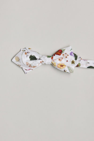 The Floral Eve Liberty Bow by Liberty is a handmade white bow tie from soft Tana Lawn cotton, showcasing a vibrant floral print with assorted flowers and leaves, photographed on a plain light grey background.