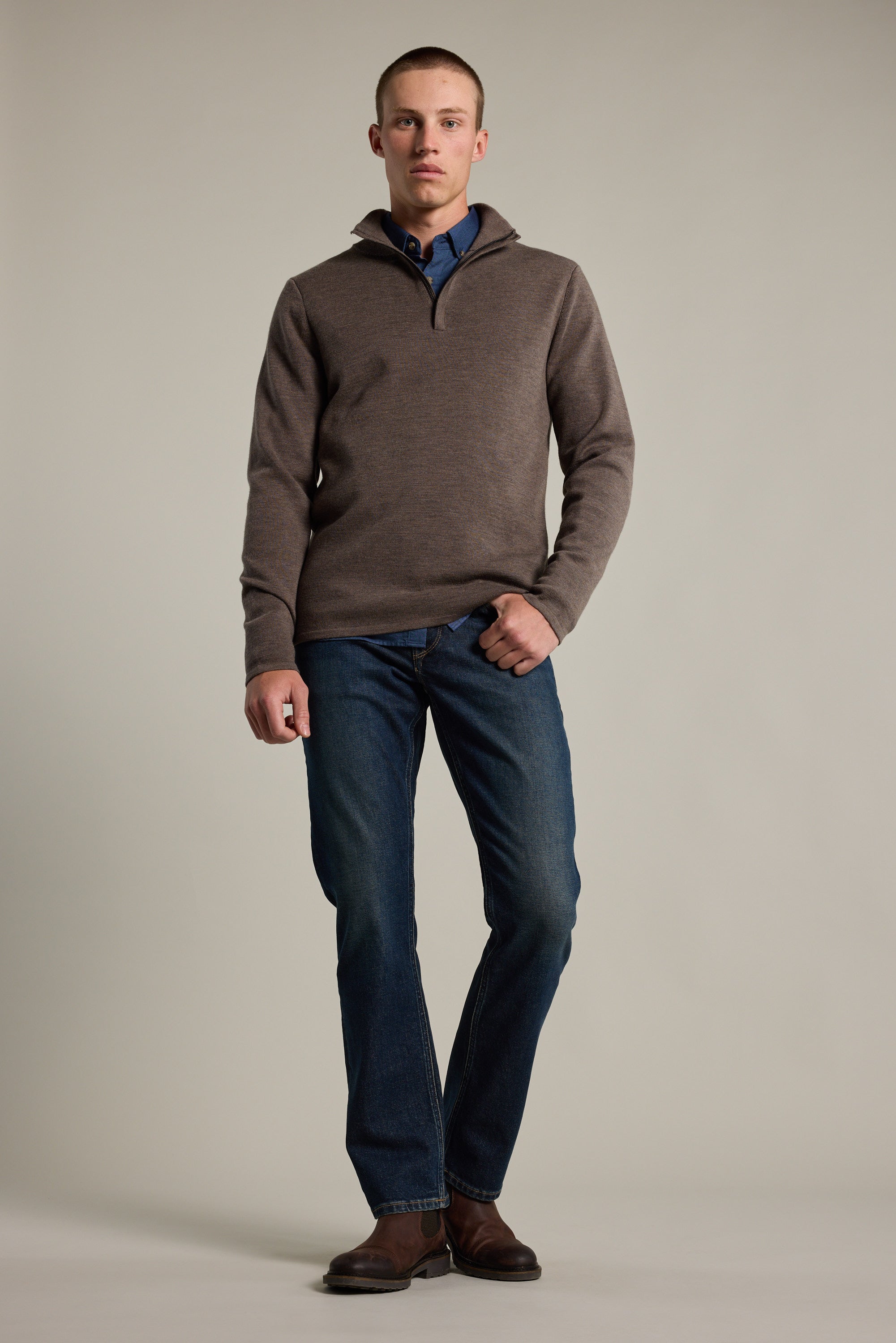 A person stands against a plain background wearing the Barkers Brandon ZQRX Merino 1/4 Zip pullover, blue collared shirt, blue jeans, and brown shoes with one hand in their pocket—ideal for cold-weather layering.