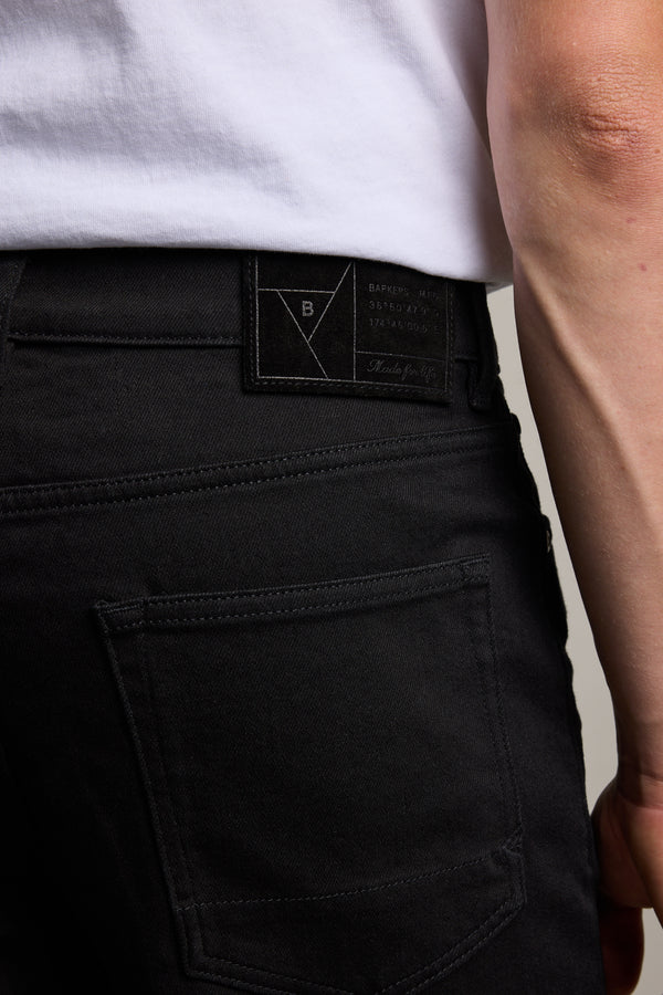 A close-up of a person wearing Barkers Rambler Denim Slim Jean—black slim fit jeans with a black label, spotlighting the back pocket and waistband, crafted from sustainable denim for modern style.