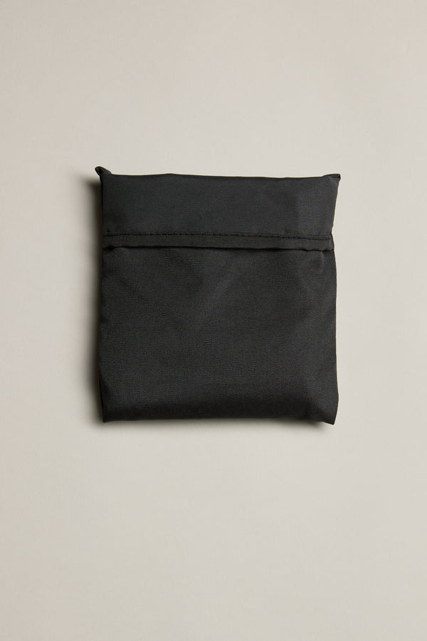 The Barkers Shopping Bag, a closed flat black bag made from recycled polyester, is shown with a horizontal flap on a plain light beige background.