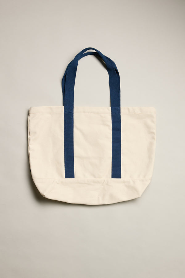 The Barkers Supply Co. Canvas Tote Bag by Barkers features dark blue handles and trim on durable canvas, photographed against a light background. This versatile travel tote's simple, unadorned design is complemented by its neatly arranged handles.