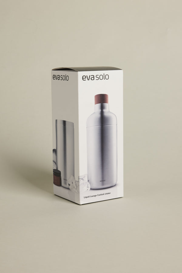 A box of Other Liquid Lounge Cocktail Shaker, a home bar essential featuring the stainless steel shaker with a wooden cap shown on the packaging front and side, set against a neutral background.