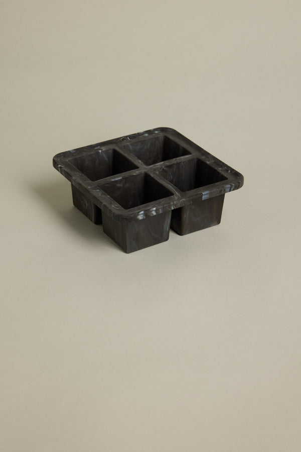 The Other Ice Tray Sphere Marble Black, a black silicone tray with four large compartments for slow-melting ice in your home bar, is set on a plain beige background.