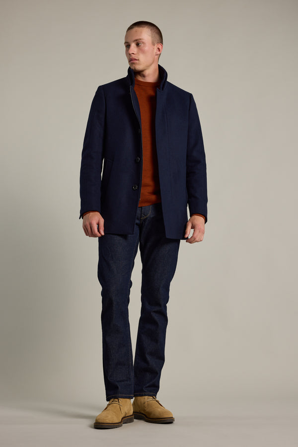 A man faces forward wearing a Barkers Raymond Coat in navy wool blend over a rust sweater, dark jeans, and tan suede shoes, set against a plain light gray background.