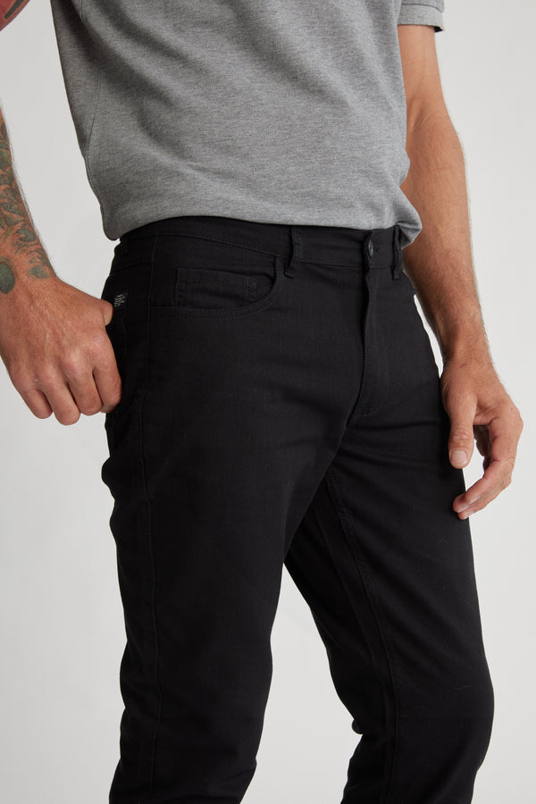 A person in a grey short-sleeve shirt and Barkers Oxmor 5 Pkt Pant O (black, taper fit) stands with a tattooed arm near their pocket. Image shows from shoulders to mid-thigh.