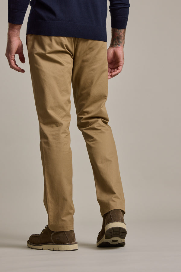 A person is seen from the back, wearing Barkers Dundas Chino trousers in lightweight cotton twill, brown shoes, and a navy sweater, standing against a plain background.