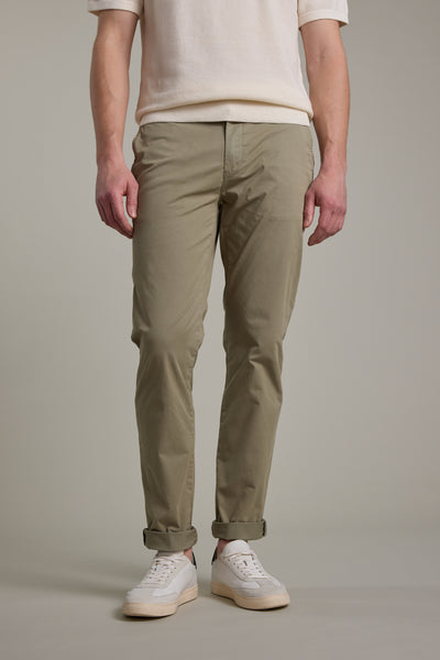 A person models Barkers Kingly Chino Pant in light khaki, paired with a white short-sleeve shirt and sneakers. The image, cropped at the shoulders, focuses on the lower half of the body against a plain background.