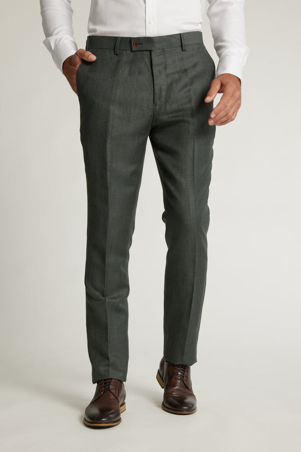 A person stands against a plain background, wearing a white dress shirt, Barkers Inverness Suit Trouser in dark gray tapered fit, and brown dress shoes, with one hand in their pocket.
