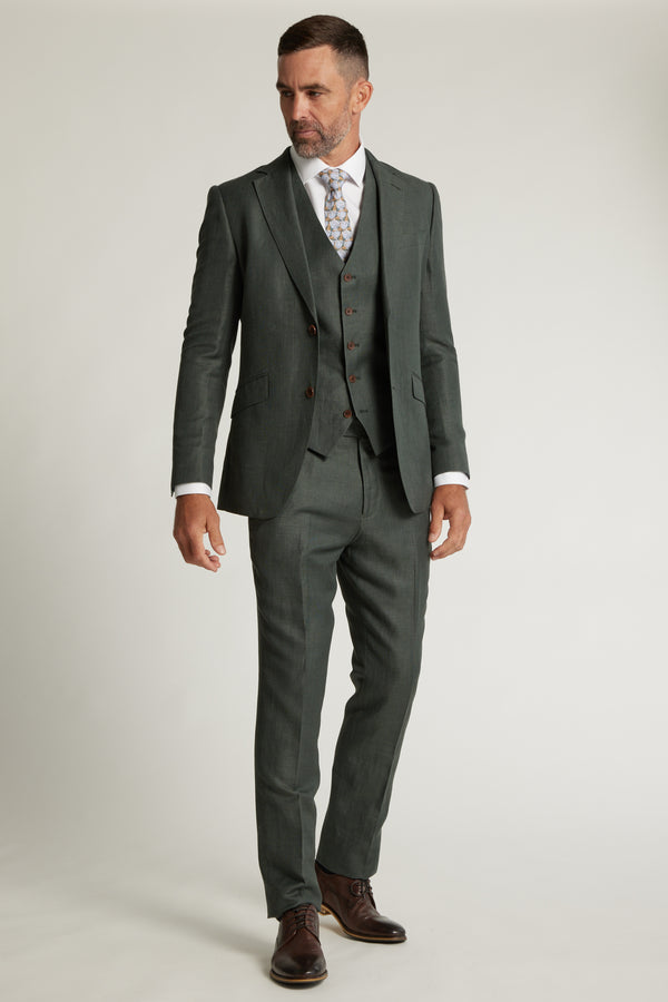 A man wears the Barkers Inverness Suit Jacket in sage green with a white shirt, patterned tie, and brown dress shoes, standing against a plain light background.