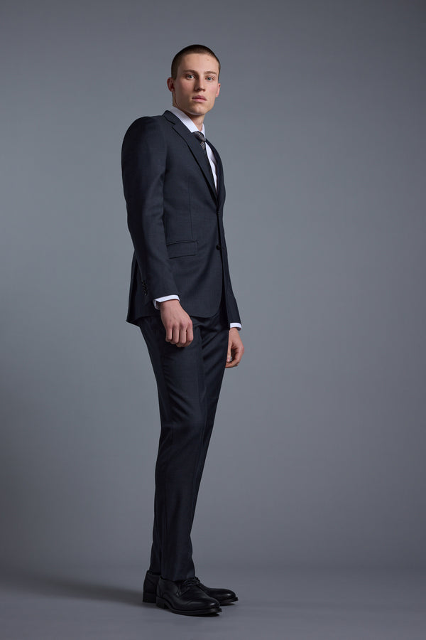 A young man in Barkers’ Mayfair ZQrx Suit Trouser, paired with a dark suit jacket, white shirt, and tie, stands against a plain gray background, gazing slightly left with a neutral expression.