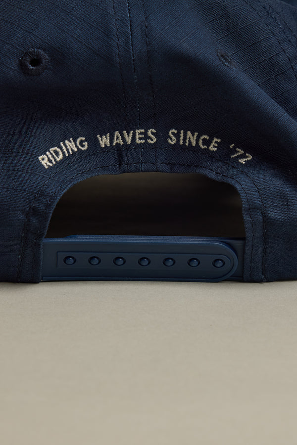 Close-up of the back of the Barkers Wave Master Cap by Barkers, showing an adjustable snapback strap and an embroidered patch with "RIDING WAVES SINCE 72" in white above the opening.