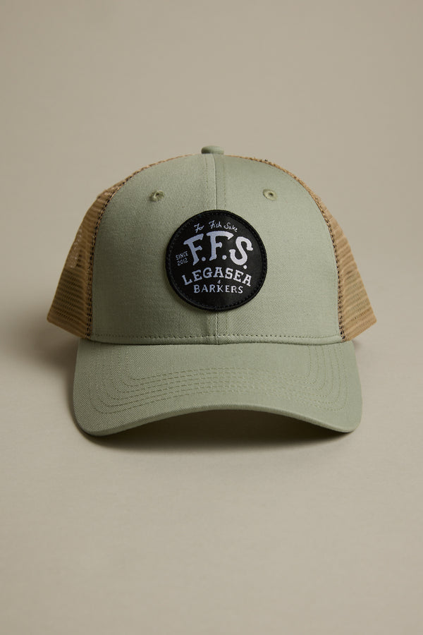 The Legasea FFS Trucker Cap by Legasea features khaki green and tan mesh with a round black patch reading “F.F.S LEGASEA BARKERS” in white, shown against a plain beige background.