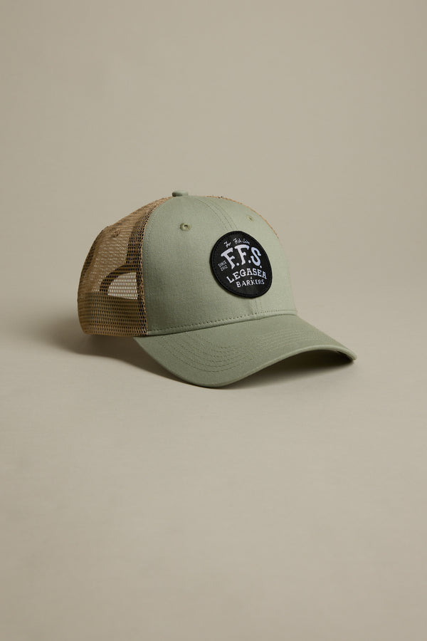 The Legasea FFS Trucker Cap features green and tan mesh with a black patch that reads "FFS Legacy Eager" in white. Displayed on a beige background, it's perfect for Legasea fans.