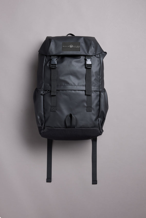 The WearEver Transit Backpack by WearEver is a sleek black bag with a top flap, two front buckles, side pockets, water-resistant zips, and a logo patch on the flap, shown upright on a plain light gray background.