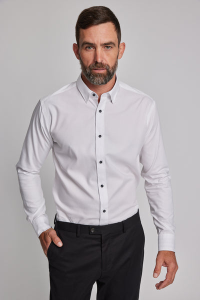A man with short brown hair and a beard wears the Barkers Verona Shirt, a tailored fit, long sleeve white business shirt in 100% cotton, paired with black pants, standing against a plain light gray background.