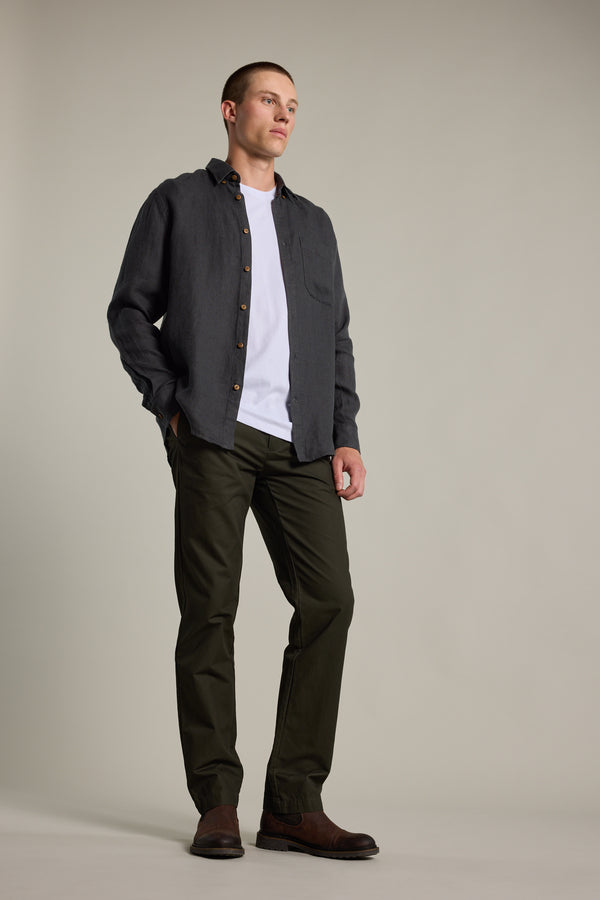 A man stands in a relaxed pose wearing the Barkers Delano Linen Shirt over a white T-shirt, paired with dark pants and brown shoes, set against a plain light background.