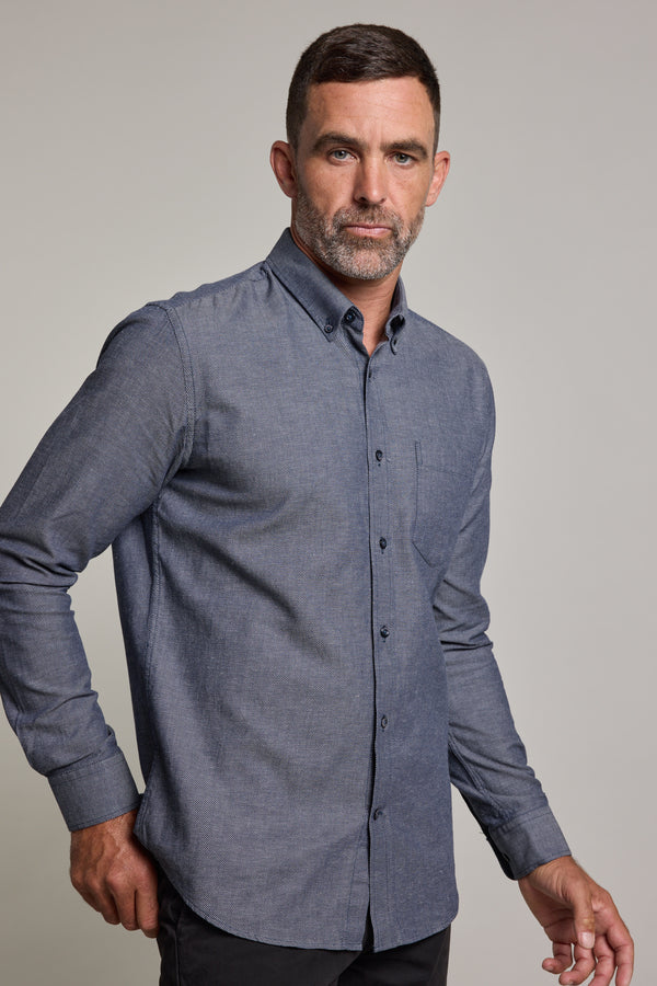 A man with short hair and a beard wears the Barkers Tyson Texture Shirt, a long-sleeved, blue-gray linen-cotton blend button-up, paired with dark pants, standing against a plain light background and looking confidently at the camera.
