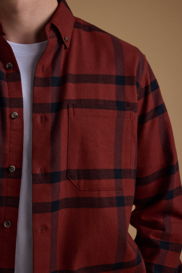A person wears the Barkers Durness Check Shirt, made from responsibly sourced cotton, over a white T-shirt. Only their upper torso and part of their face are visible against a plain brown background.