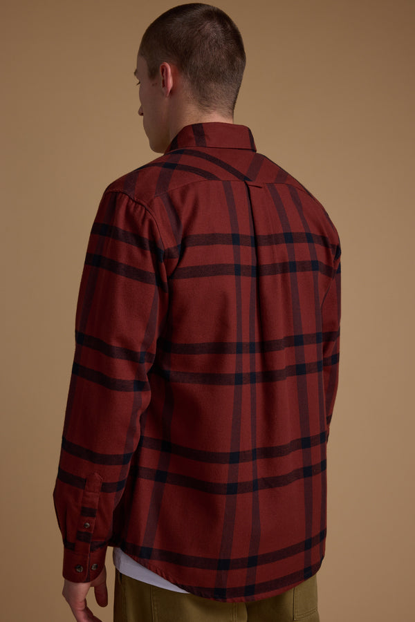 A person stands with their back to the camera, wearing a red Durness Check Shirt by Barkers over a white shirt and olive pants, against a plain brown background. The flannel shirt is made from responsibly sourced cotton.