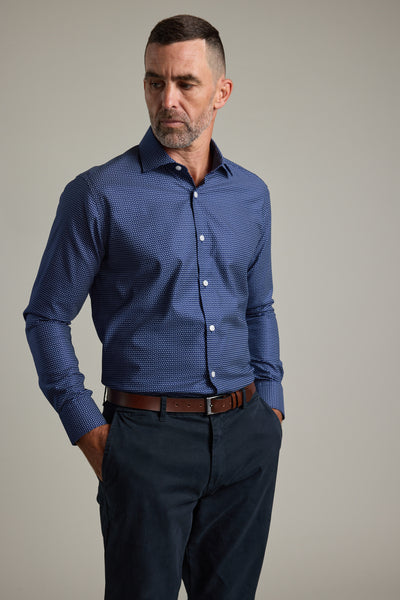 A man with short dark hair and a trimmed beard wears the Barkers Maiden Paisley Business Shirt in navy, paired with dark trousers and a brown belt. He stands hands in pockets, looking to the side against a plain background.