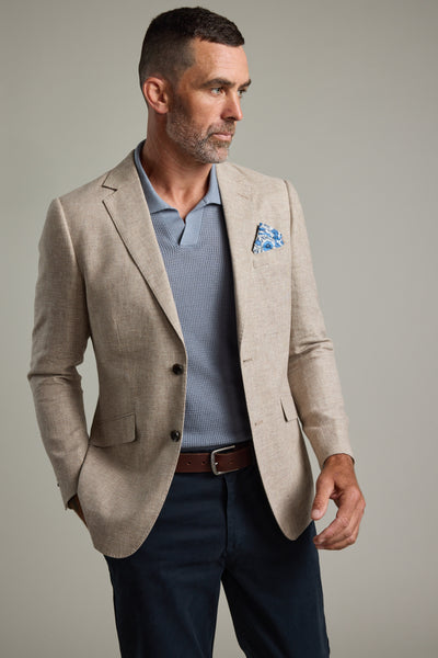 A man with short dark hair and a beard wears the Barkers Welland Texture Blazer over a light blue shirt, dark trousers, and a brown belt with a patterned blue pocket square, standing against a plain light background.