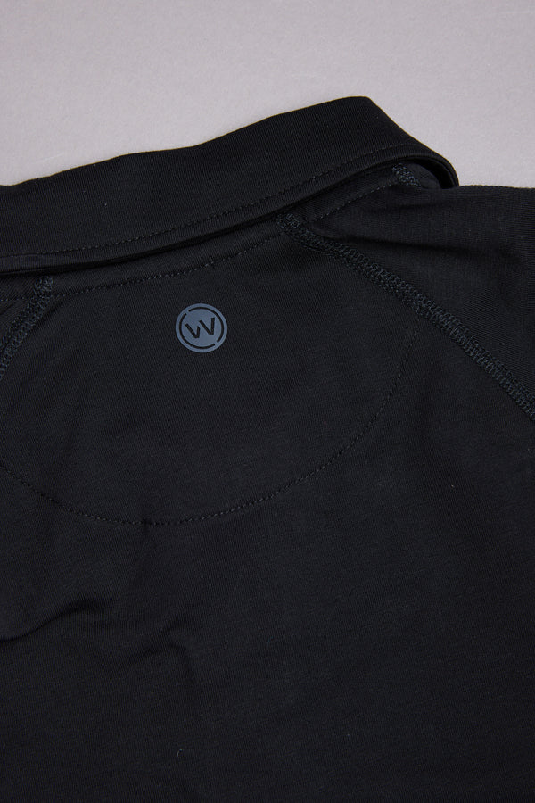 Close-up of the back of a black WearEver Outbound Polo, showcasing a small circular "W" logo near the neckline. Breathable cotton-blend fabric and stitching details highlight its lightweight stretch comfort.