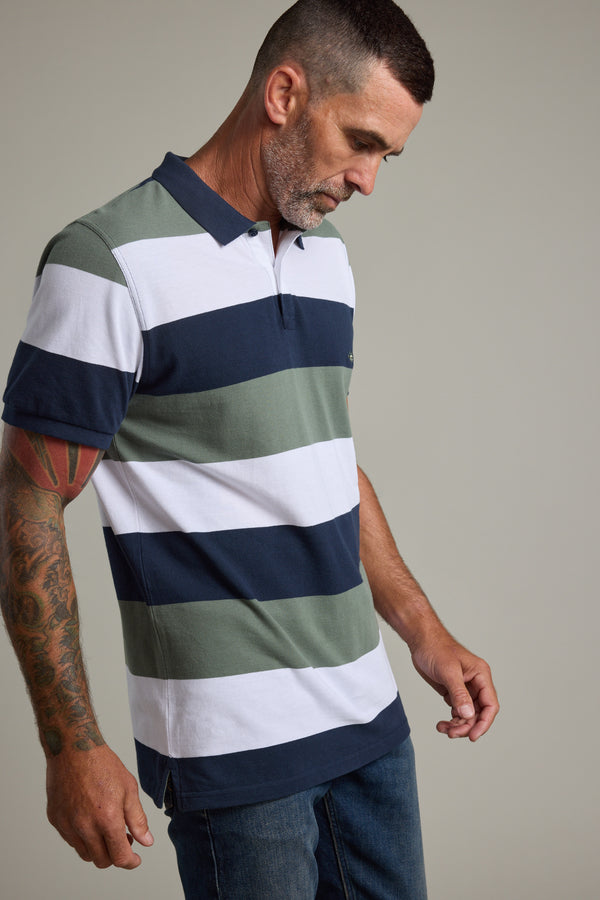 Tattooed man in Barkers Regent Pique Stripe Polo stands against a plain background.