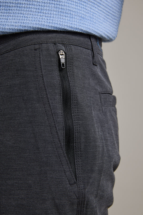 Close-up of a person wearing Barkers Hutchinson Walkshorts in dark gray four-way stretch fabric with a side zippered pocket, paired with a light blue textured knit sweater.