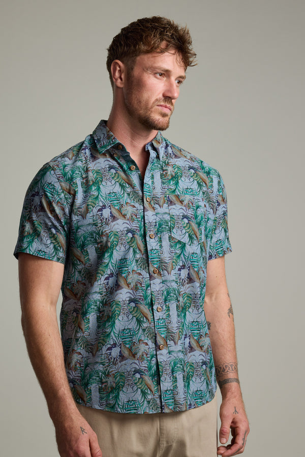 A man with short brown hair and stubble wears a Barkers Rockport Print Shirt with a tropical pattern, styled as a summer party shirt with beige pants, standing against a plain light gray background.