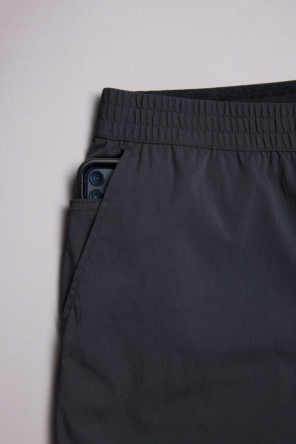 The WearEver Transit Pant by WearEver is a black, lightweight travel pant with an elastic waistband, shown on a plain background. A smartphone peeks out from the pant’s side pocket.