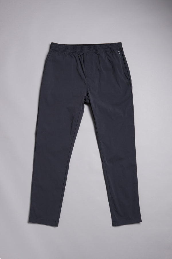 The WearEver Transit Pant by WearEver is a pair of dark navy blue lightweight track pants with an elastic waistband, side pockets, and a relaxed fit, shown laid flat on a light gray surface.
