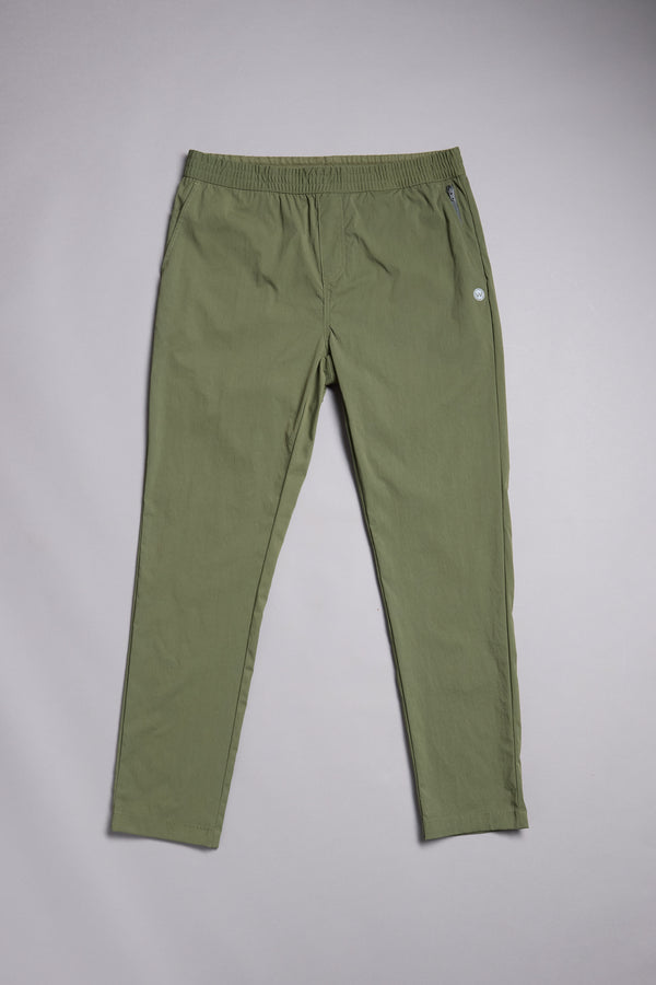 The WearEver Transit Pant by WearEver, in olive green, features a slim fit, elastic waistband, and buttoned side pocket; shown laid flat on a plain light gray background.