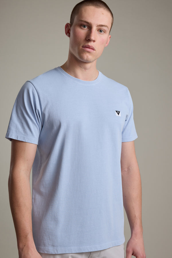 A young man with short hair wears the Barkers Newton Washed Tee, an oversized box fit t-shirt in light blue with a small black and white logo on the left chest, standing against a plain light gray background.