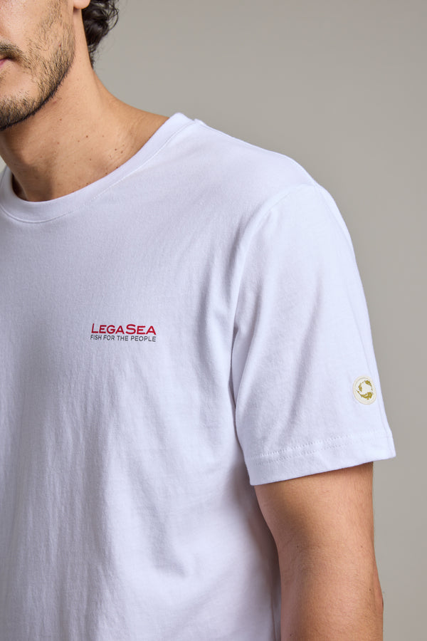 A person wears the Legasea Brand Tee—made from organic cotton, featuring bold red “LEGASEA FISH FOR THE PEOPLE” text on the chest and a small circular Legasea logo on the sleeve. Only their upper torso and part of the face are visible.