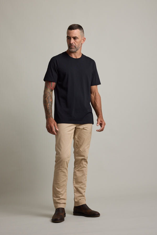 Man in Barkers Good Earth Cotton Essential Tee, beige pants, and brown boots on plain background.