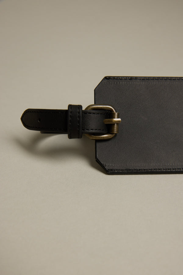A close-up of the Barkers Voyage Leather Luggage Tag in black, featuring a brass buckle and displayed on a beige surface—a stylish essential for frequent flyers.