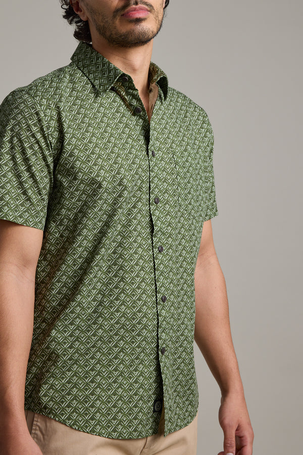 A man wears the Barkers Oxnard Print Shirt in green organic cotton with beige pants, standing against a plain background. His face is partially out of frame.