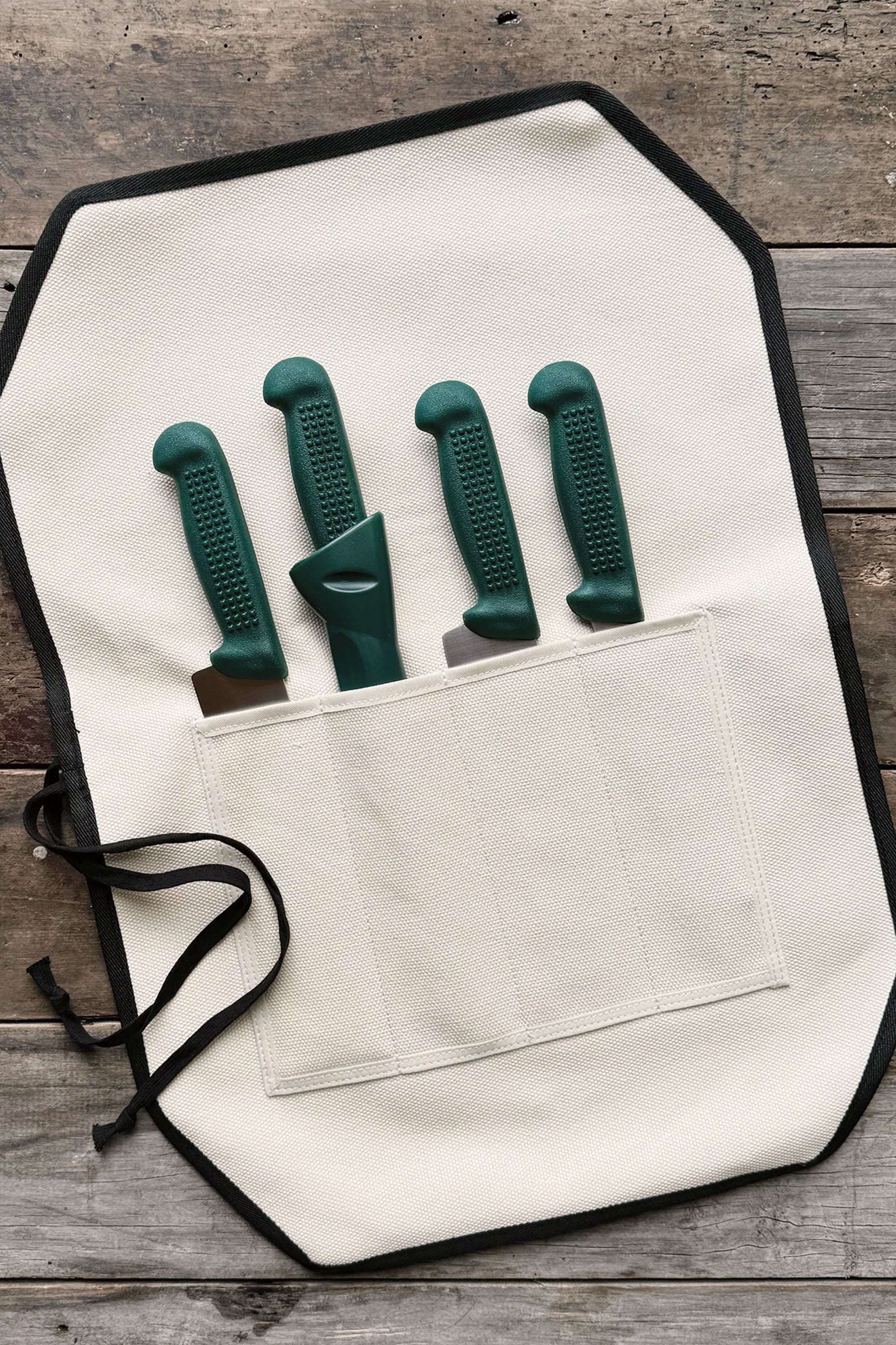 The IronClad Ghost Knife Roll is a limited edition white canvas roll, shown open on wood, with four green-handled knives partly visible in separate pockets.