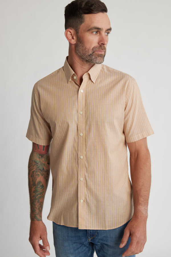 A man with short brown hair and a beard wears the Barkers Burnham Stripe Shirt and blue jeans. He has a colorful tattoo on his left forearm and looks to his left against a plain background.