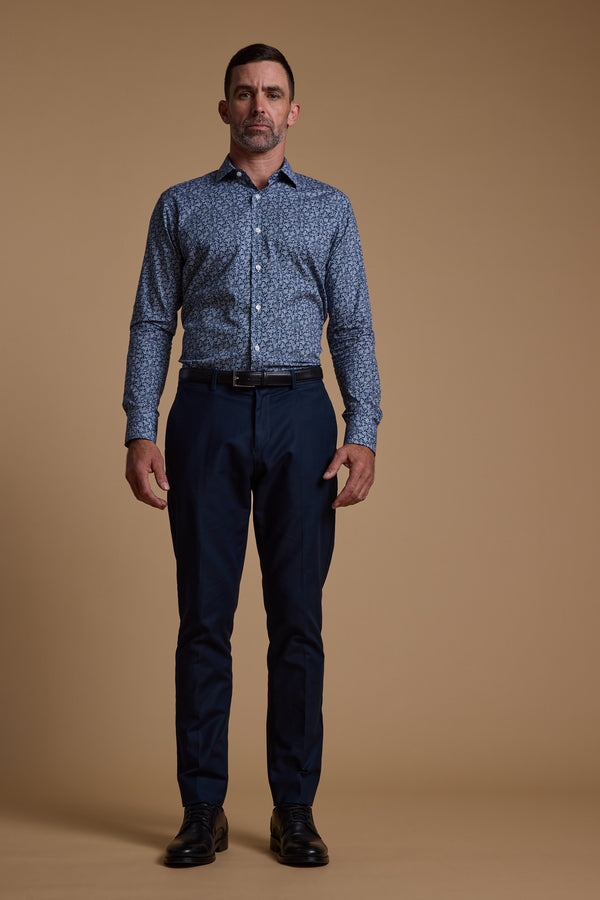 A man stands facing forward against a plain beige background, wearing the Barkers Watkins Print Business Shirt, paired with dark blue trousers, a black belt, and black dress shoes.