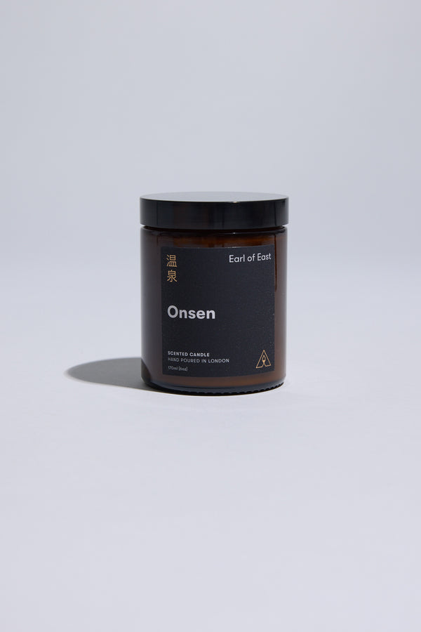 The 170ml EoE Onsen Candle by Earl of East, in a dark amber glass jar with black lid and minimalist gold and white English/Japanese text, is shown against a plain light gray background.