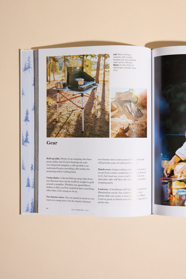 An open magazine displays a page featuring Camping Life gear by Other, including a folding table with grill and fire pit, with text descriptions. The background is a light beige surface.